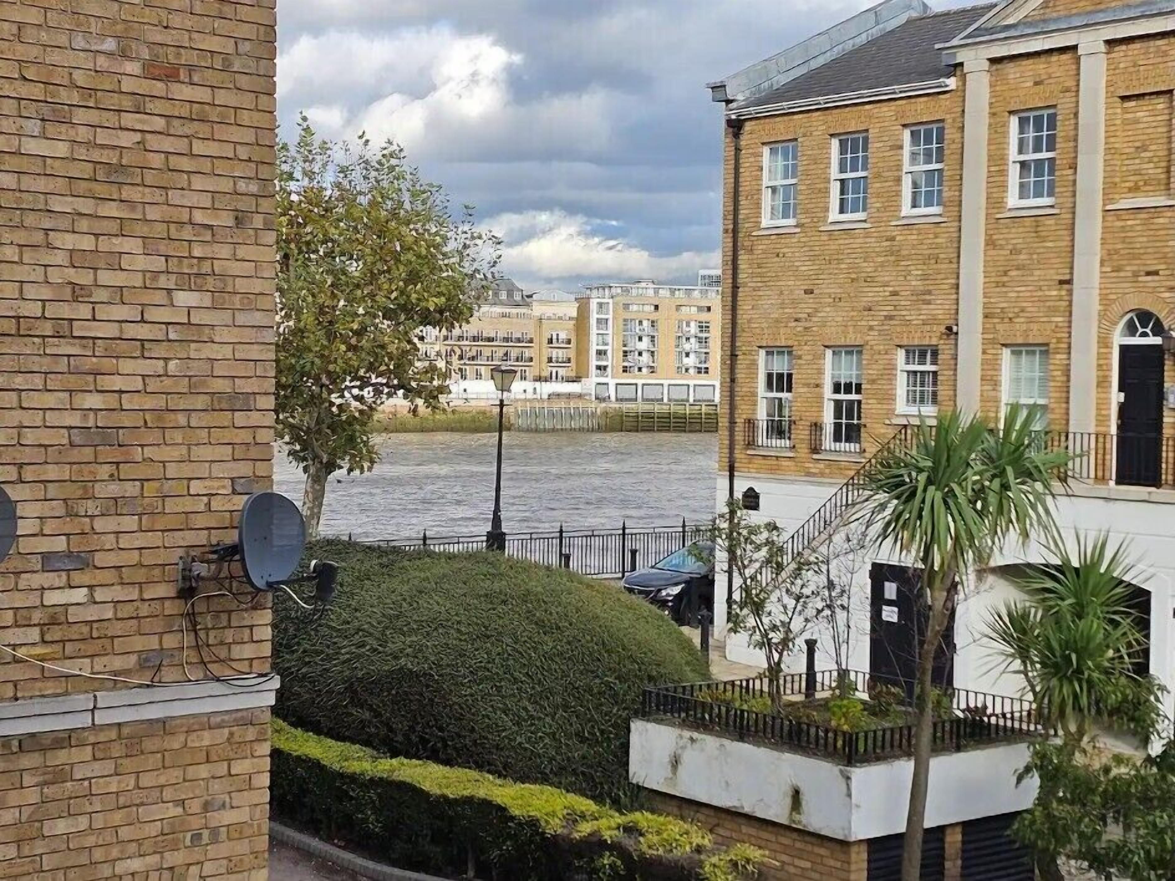 Un edificio residencial con fachada de ladrillo, una puerta blanca y un pequeño jardín con un árbol y un seto.