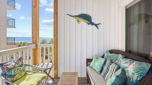 Un balcone con vista sull'oceano, un divano in vimini con cuscini decorati e un tavolo in legno.