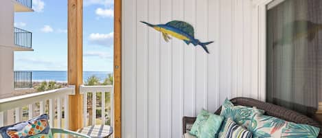 A balcony with a view of the ocean, a wicker sofa with patterned cushions, and a wooden table.