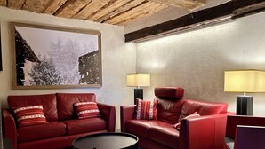 A room with a red leather sofa, a round coffee table, and two floor lamps. A framed picture of a snowy landscape is on the wall. - HAUTE-NENDAZ VILLAGE: LARCH 1898 4-STOREY/4-ROOM/6-PERSON CHALET/PARKING. (Nendaz)