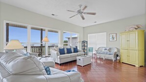 A spacious living room with a white sofa, a white armchair, a yellow cabinet, and a ceiling fan. - Sound Front Home with both Gulf & Sound Views! (Dauphin Island)