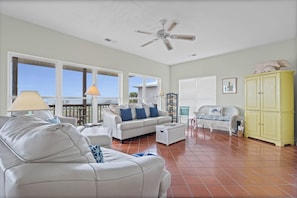A spacious living room with a white sofa, a white armchair, a yellow cabinet, and a ceiling fan.