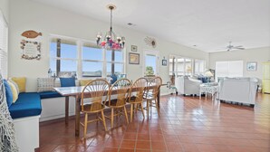A spacious living area with a dining table, chairs, a sofa, and a view of the outdoors. - Sound Front Home with both Gulf & Sound Views! (Dauphin Island)