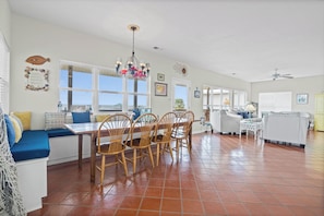 A spacious living area with a dining table, chairs, a sofa, and a view of the outdoors.
