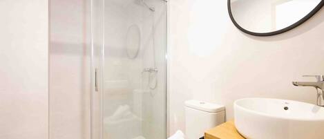 A modern bathroom with a glass-enclosed shower, a white toilet, and a wooden vanity with a large sink.
