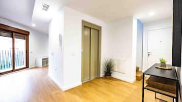 A spacious room with wooden flooring, a sliding glass door, a small table with a plant, and a door with a light switch.