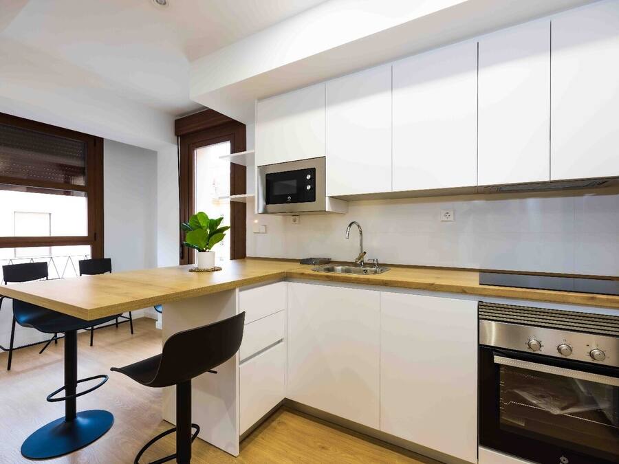 Una cocina moderna con armarios blancos, encimera de madera, microondas, fregadero y horno empotrado.