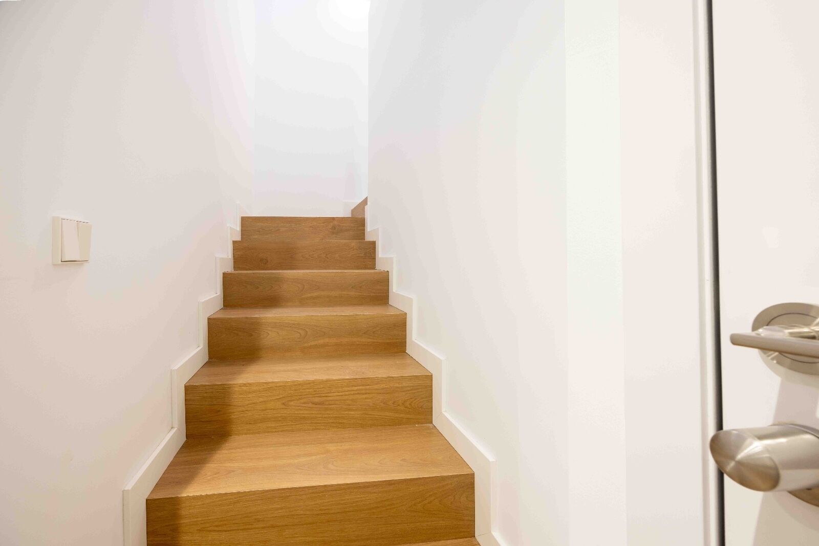 A narrow, wooden staircase leading to a landing with a white door.