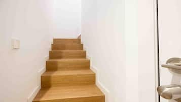 Een smalle houten trap die uitkomt op een plateau met een witte deur.