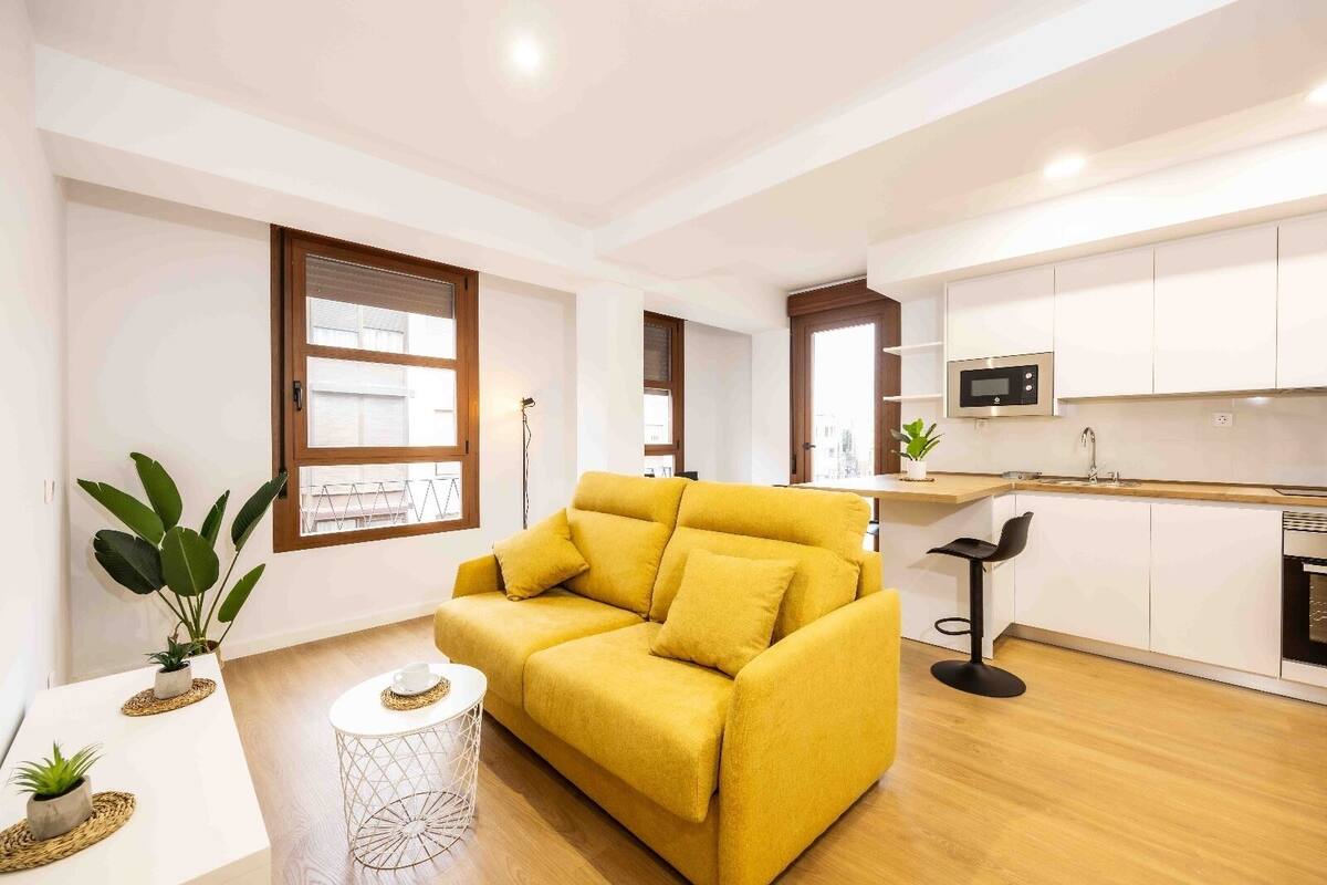 Una sala moderna con un sofá amarillo, una mesa de centro y plantas en macetas.