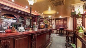 A bar area with a wooden counter, bar stools, and a decorative plant. - Hôtel Le Celtic (Le Thillay)