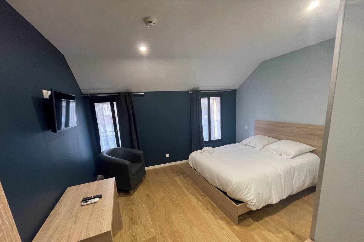 A bedroom with a bed, a desk, a chair, and a window.