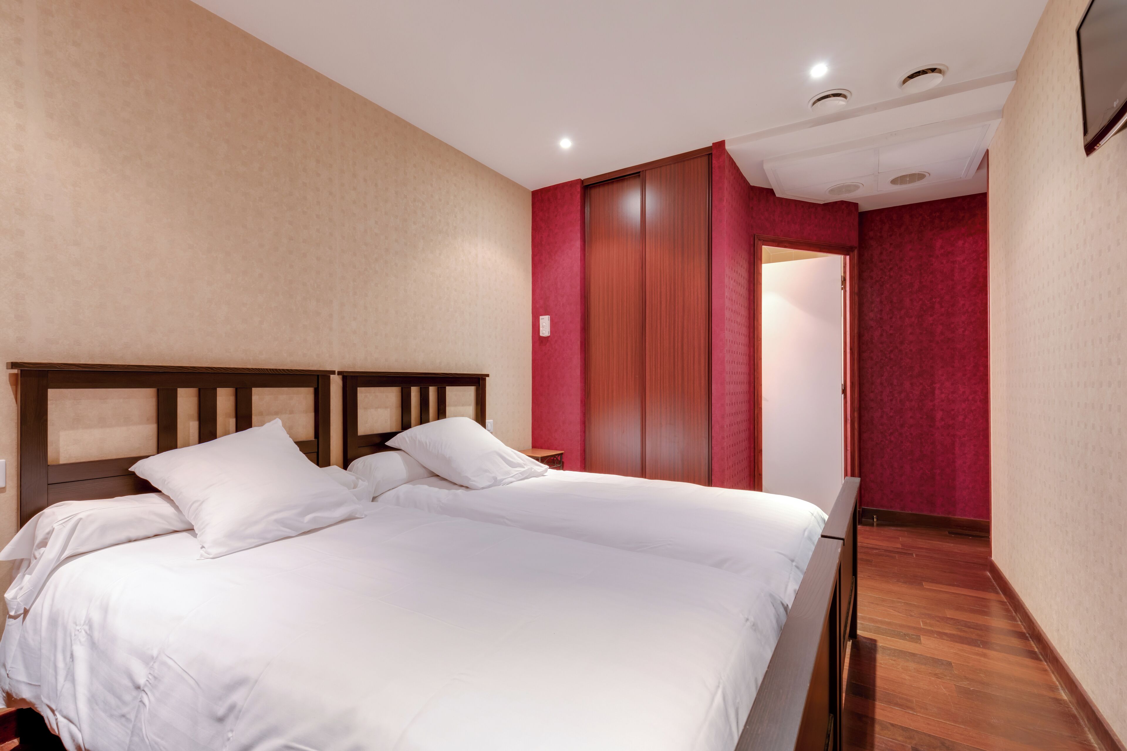 Quarto com cama de madeira, parede em vermelho e guarda-roupa de madeira.