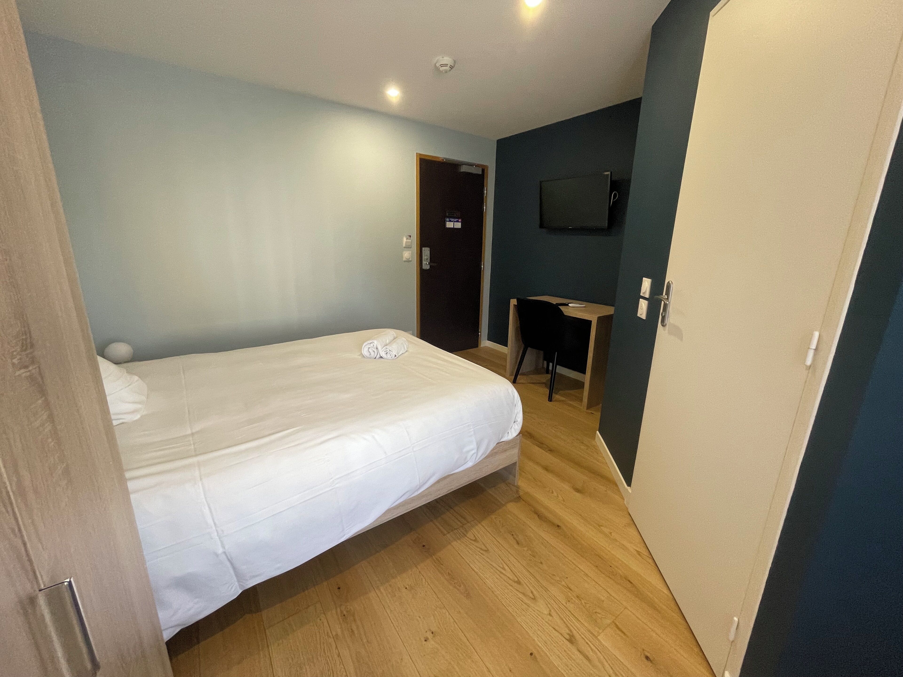 Una habitación de hotel con cama, escritorio y televisor instalado en la pared.