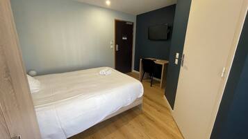 Una habitación de hotel con cama, escritorio y televisor instalado en la pared.