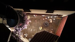 An outdoor patio area with a wooden floor, seating arrangements, and string lights. - Hôtel Le Celtic (Le Thillay)