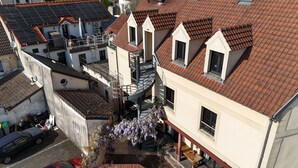 A multi-story building with a spiral staircase, a small garden with purple flowers, and a red car parked outside. - Hôtel Le Celtic (Le Thillay)