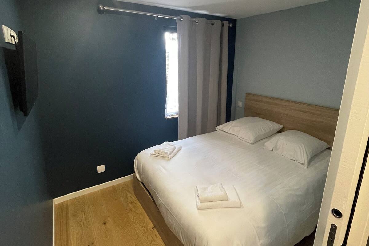 A bedroom with a bed, wooden floor, and a window with curtains.