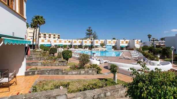 A hotel with a swimming pool, outdoor seating, and a view of other buildings.