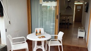A patio with a round table and two chairs, a tiled floor, and a sliding glass door leading to a kitchen area.