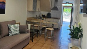 A compact kitchen with a dining area, a sofa, and a TV on the wall.