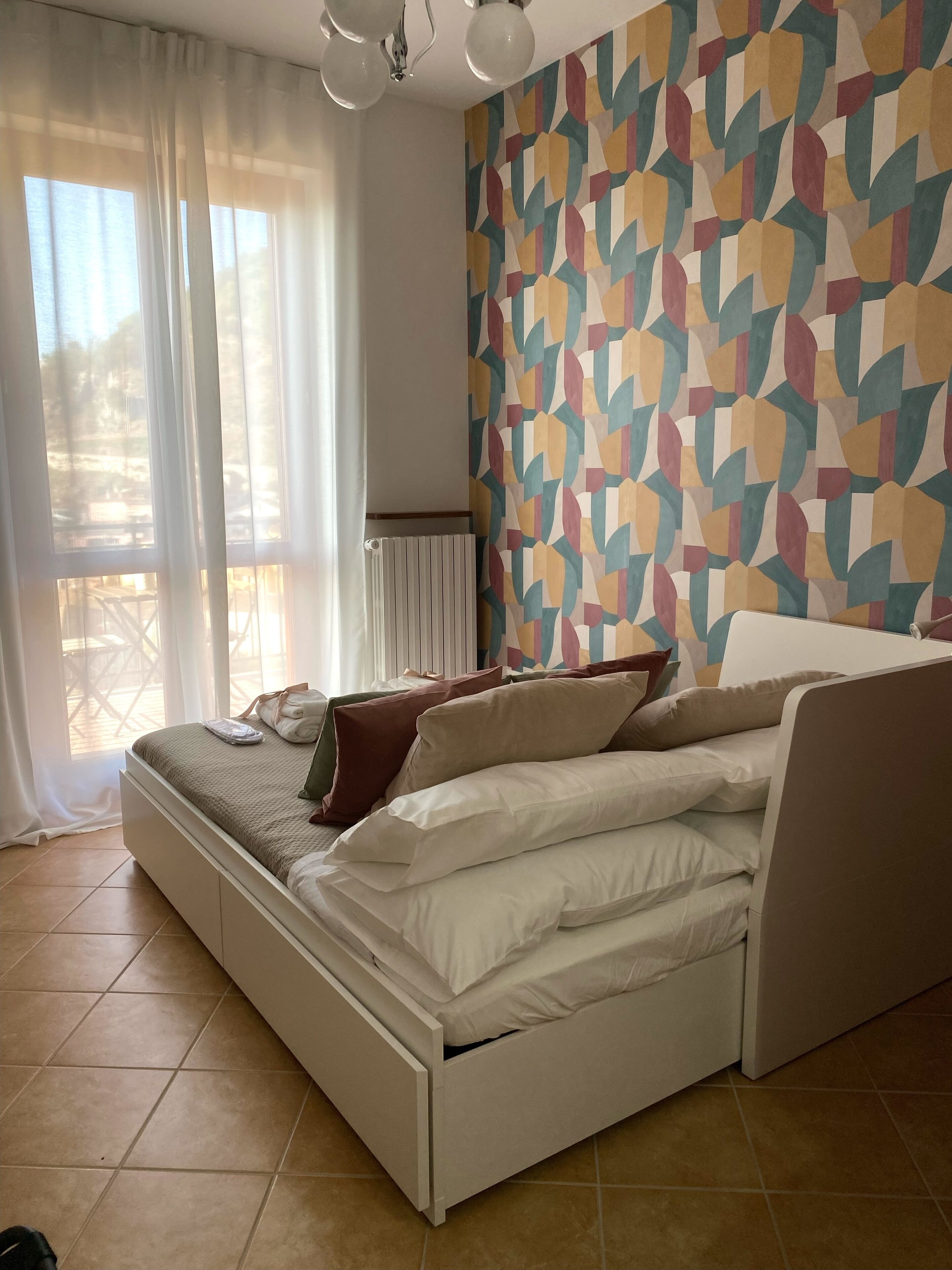 A bedroom with a bed, a patterned wall, and a window with curtains.
