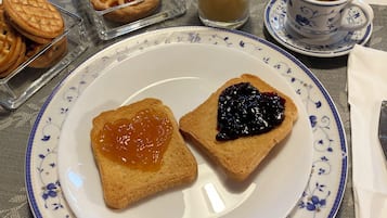 A breakfast setting with toast, jam, a glass of juice, a bowl of fruit, and a tray of pastries.