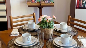 Una mesa de comedor dispuesta con tazas, platillos y platos blancos, rodeada de individuales tejidos. Una cesta con flores está colocada en el centro.
