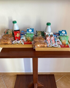 Una mesa de madera con dos bandejas de alimentos, incluyendo pan, galletas y bocadillos envasados.