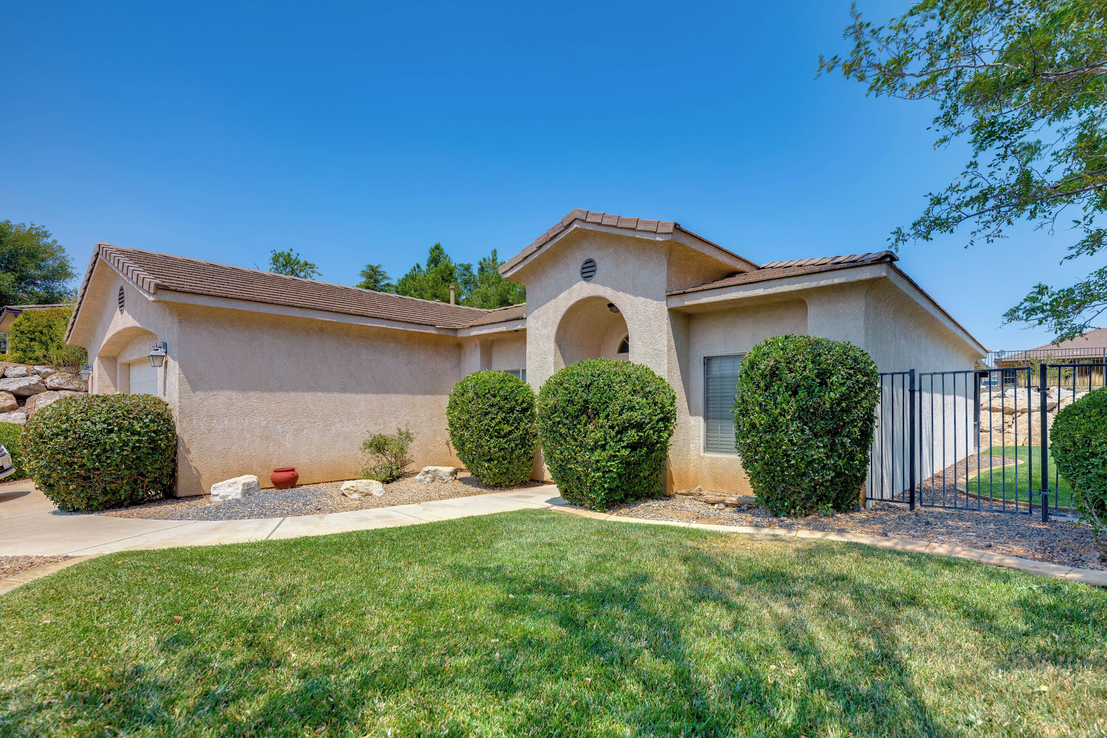 A single-story house with a stucco exterior, a tiled roof, and a front yard with trimmed hedges and a small red pot.