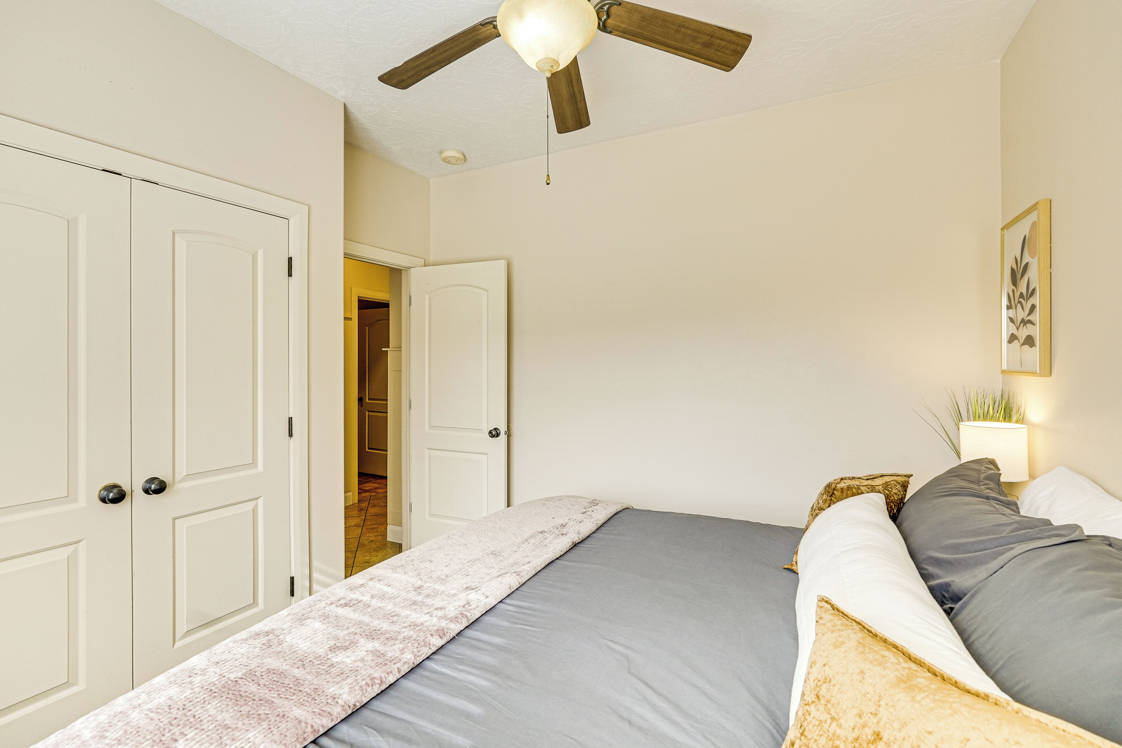Un dormitorio con cama, ventilador de techo y puerta que da a otra habitación.