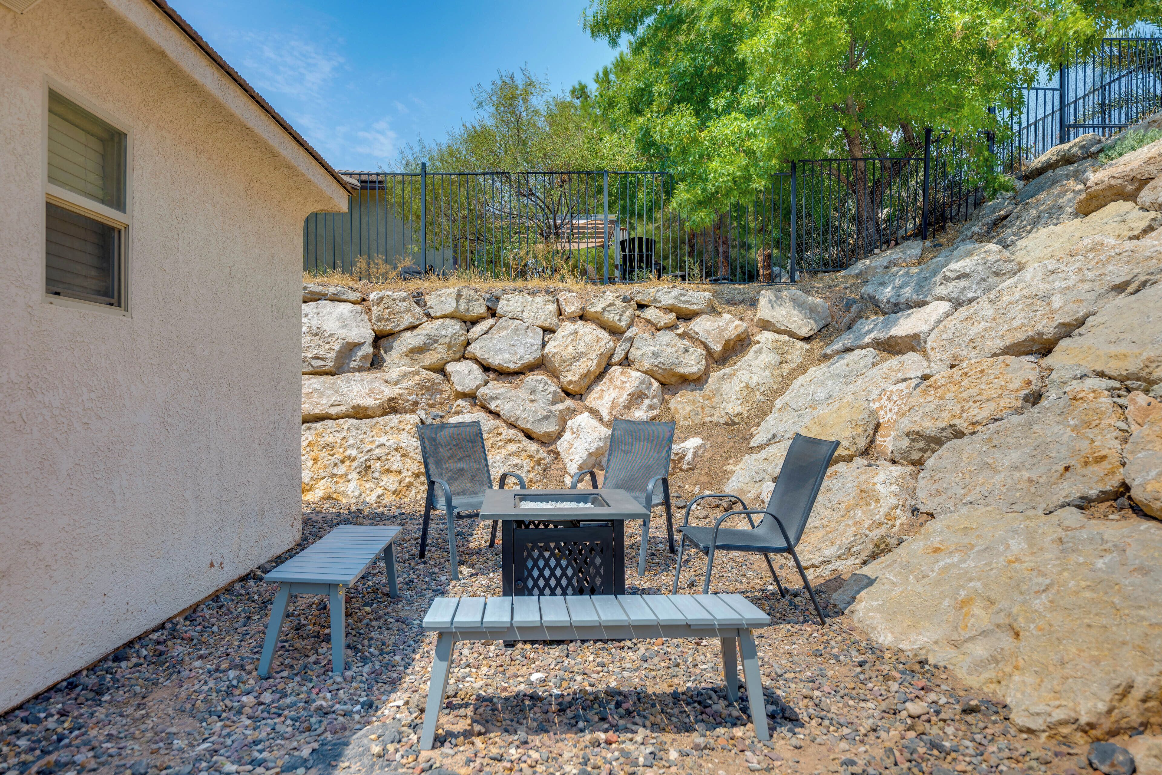 Un patio al aire libre con una mesa y cuatro sillas, rodeado por un muro de piedra y una cerca.