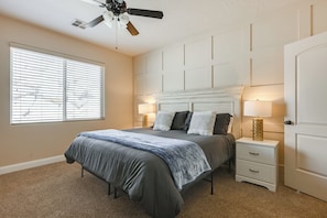 A bedroom with a bed, nightstands, a ceiling fan, and a window with blinds.