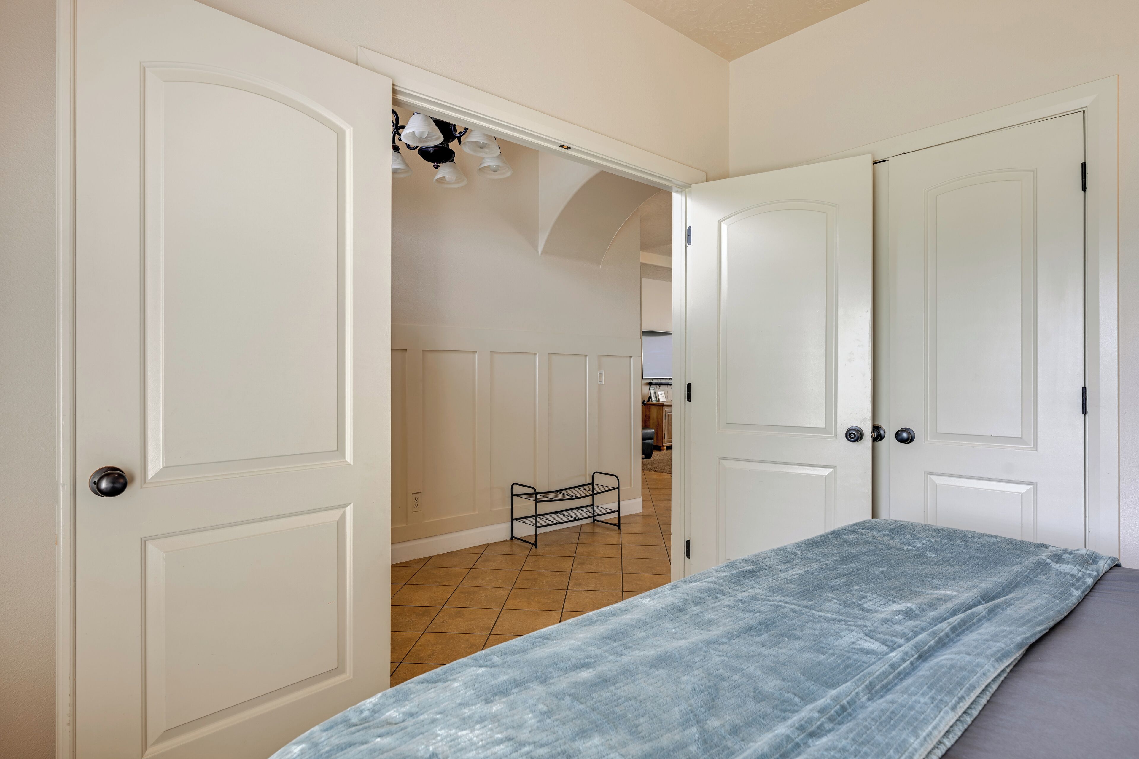 A room with a bed, white doors, a tiled floor, and a kitchen in the background.