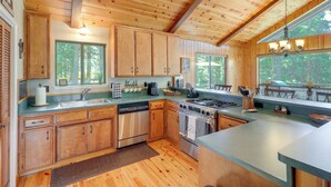 A wooden cabin kitchen with a dishwasher, stove, and large windows. - Quiet Cabin w/ Deck: Near Lake Almanor! (Westwood)