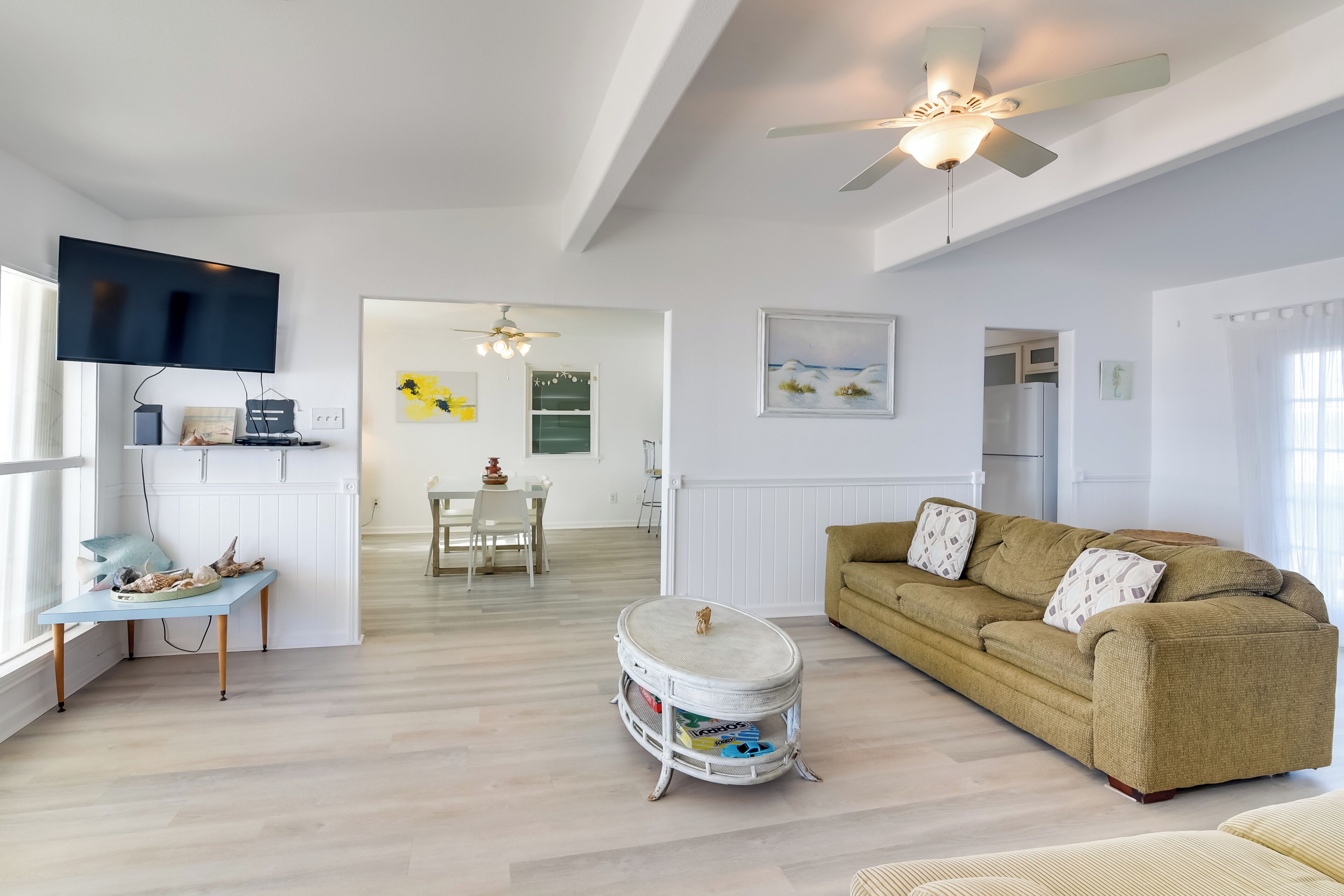 A spacious living room with a sofa, a television, and a dining area in the background.