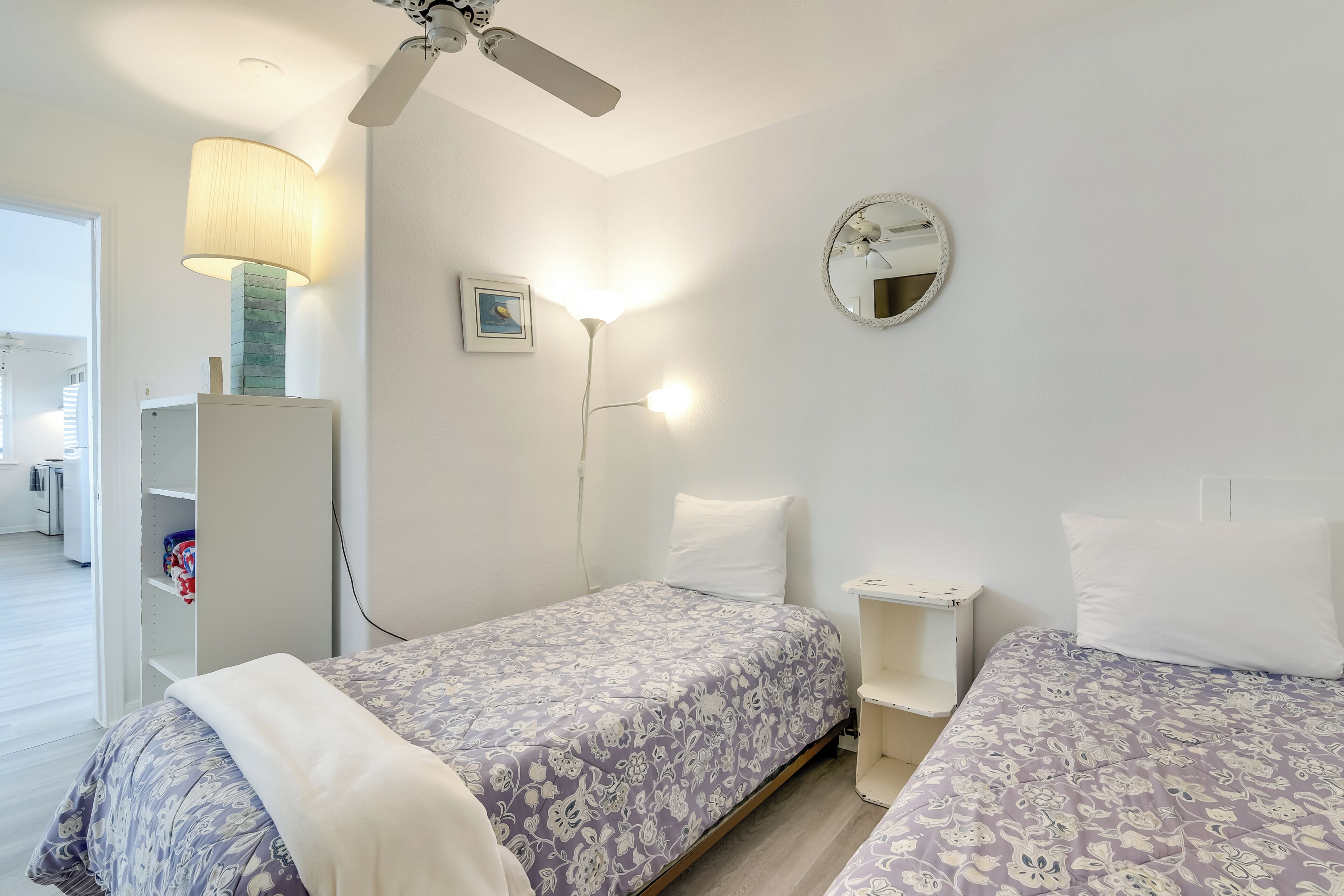 A bedroom with two beds, a ceiling fan, a bedside lamp, a mirror, and a wardrobe.