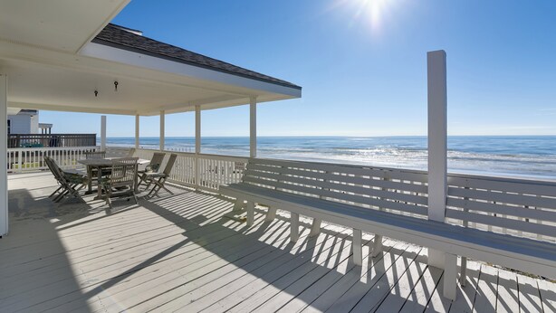 A wooden deck with a table and chairs, overlooking the ocean.