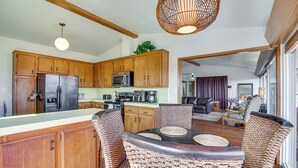 A spacious kitchen with wooden cabinets, a refrigerator, and a microwave. There is a dining area with wicker chairs and a table. - Mt. Nebo Oasis in La Mesa w/ Wraparound Deck (La Mesa)