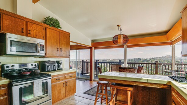 A kitchen with wooden cabinets, a microwave, an oven, and a large window overlooking a balcony. - Mt. Nebo Oasis in La Mesa w/ Wraparound Deck (La Mesa)