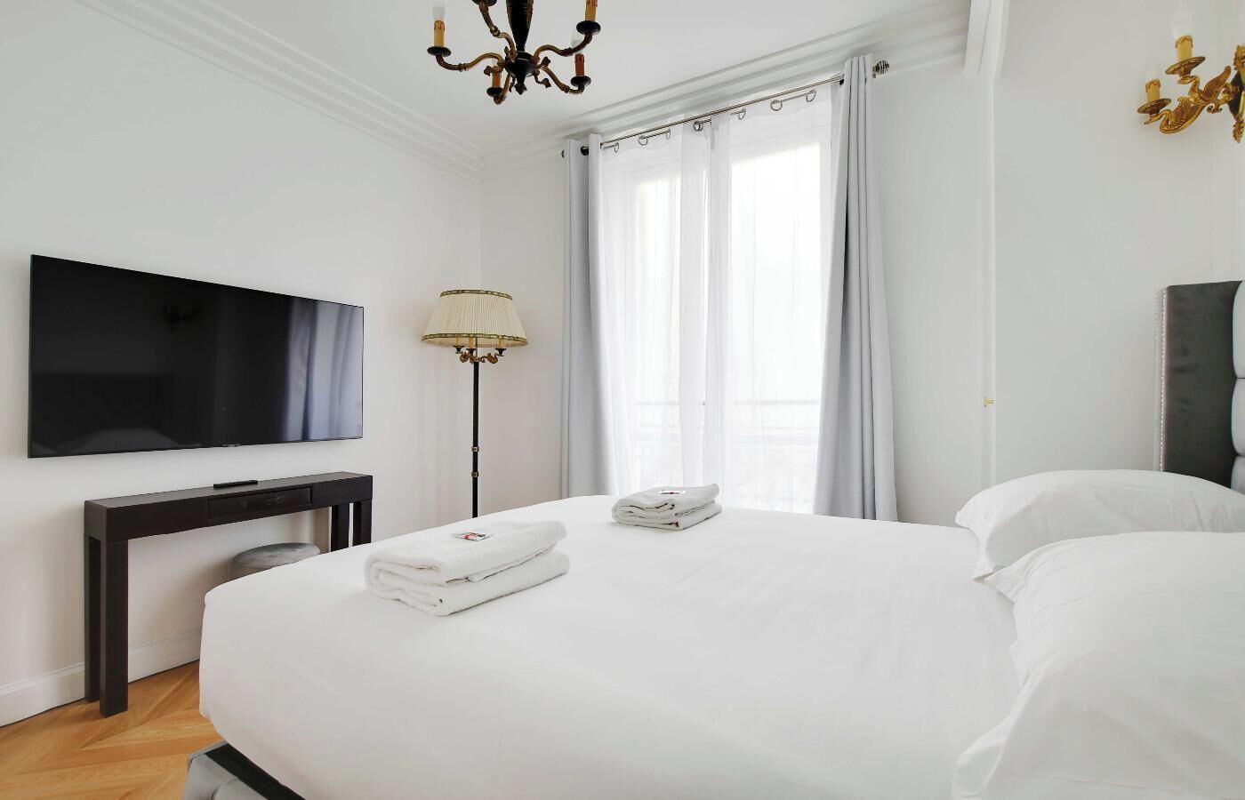 A hotel room with a large bed, a flat-screen TV, a desk, and a floor lamp.