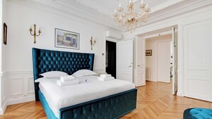 Une chambre spacieuse avec un grand lit, du linge de lit blanc et une tête de lit bleue recouverte de tissu.
