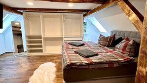 Una camera da letto con soffitto a vista in stile loft, travi in legno, un letto con biancheria a quadri e un tappeto bianco soffice.