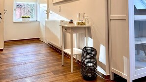 Un interno moderno caratterizzato da travi in legno a vista, un termosifone bianco, un tavolo in vetro con oggetti decorativi e un cesto in fibra nera.