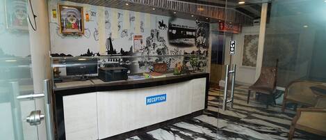 A reception area with a marble floor, a reception desk labeled "RECEPTION," and a wall decorated with various black and white images and a framed picture.