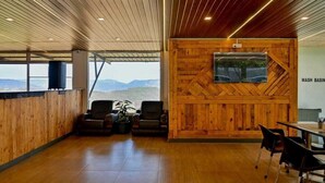 Une pièce spacieuse avec un plafond et des murs en bois, une grande fenêtre offrant une vue sur les montagnes et un téléviseur fixé au mur.