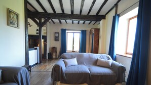 A room with a large sofa, a wooden floor, and a window with curtains. - Charming Hydrangea Cottage 3 stars, with lovely views of the countryside and hills, quiet and locate (Savignac-Lédrier)