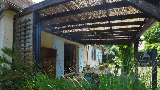 A covered outdoor area with a wooden pergola, a stone wall, and a garden with tall grasses. - Charming Hydrangea Cottage 3 stars, with lovely views of the countryside and hills, quiet and locate (Savignac-Lédrier)