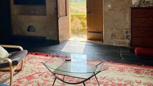 Una habitación rústica con vigas de madera a la vista, una mesa de vidrio, un tapete rojo estampado y un aparador de madera.