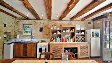 Une cuisine rustique avec des poutres apparentes, des murs en pierre et divers appareils de cuisine et meubles de rangement.